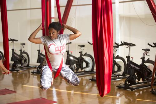 A student does a yoga pose hanging from silks during an aerial yoga group fitness class. 