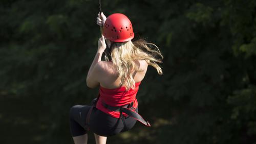 A student wearing safety gear ziplines on the Challenger ropes course