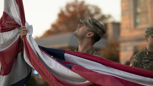 A military student helps remove an American flag during a flag retirement ceremony.