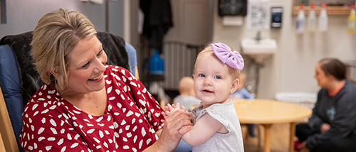 A teacher holds a baby wrapped in a swaddle blanket in a nursery room at USYC. 