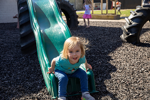 The USYC director interacts with a child sitting at a table and eating a snack in one of the classrooms.