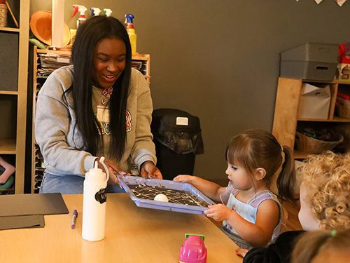 A teacher plays with a little kid at a table.