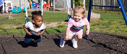Two little girls having their stomachs on the swings.