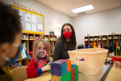 Emily Dorsam, lab student at the USYC, sits and interacts with the two children sitting at a table next to her while they build with toys.